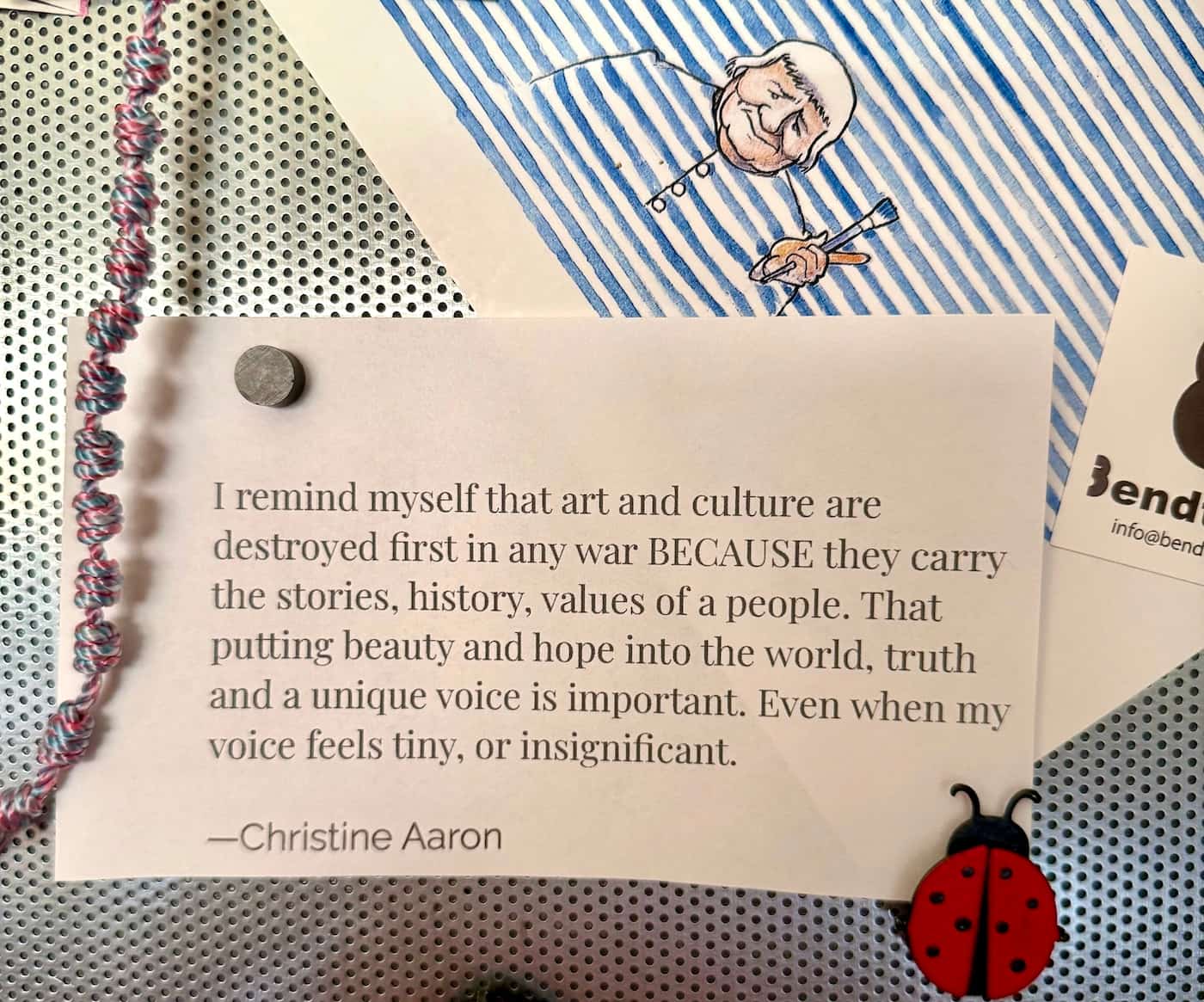 Bulletin board with an illustration of artist Agnes Martin, quote about the importance of art, and ladybug magnets.
