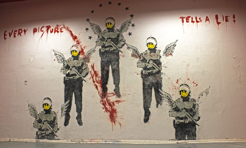 Banksy Berlin wall with armed figures, yellow faces, wings and red lettering
