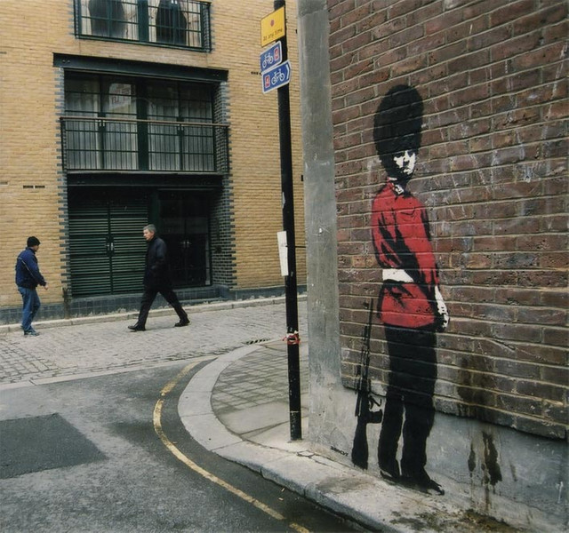 Banksy stencil of a royal guard in a red tunic on a London brick wall