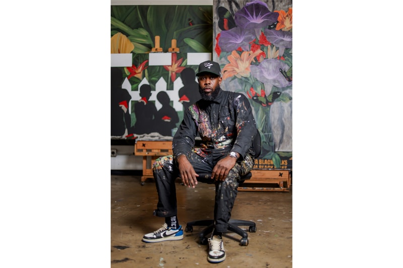 Jammie Holmes seated in his studio with paintings behind him